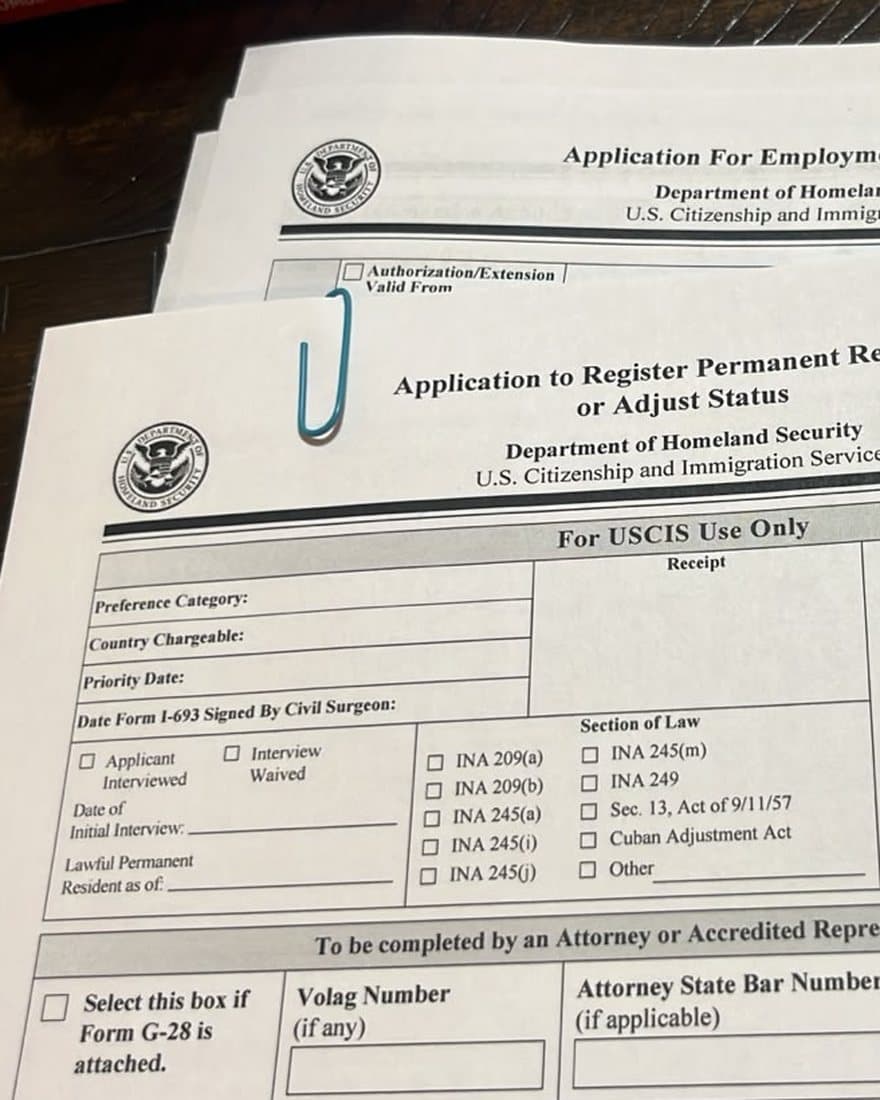 Formularios I-765 e I-485 de USCIS sobre la mesa, listos para armar